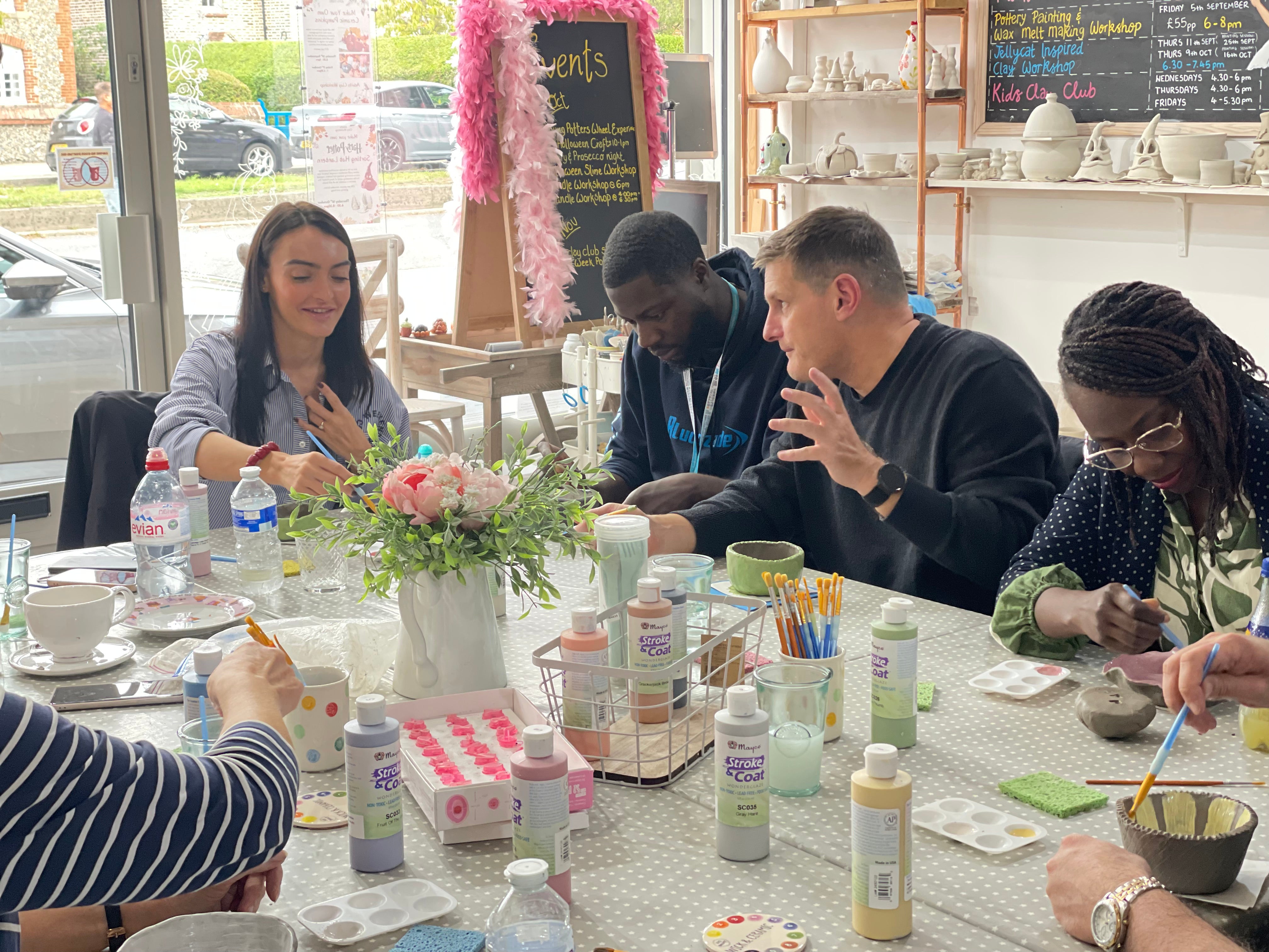 Group of people at a pottery making and painting event with art supplies on a table.