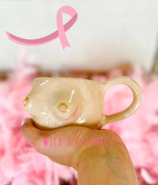 Mug designed to look like a breast with a pink ribbon on a pink background, featuring the brand 'WICK & CERAMIC'.