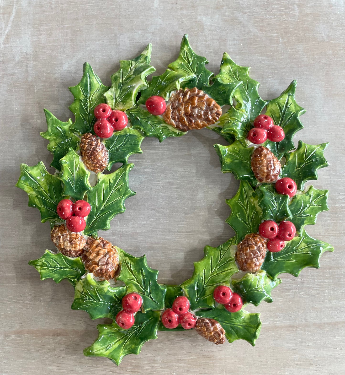 Decorative ceramic Christmas wreath with holly leaves, berries, and pinecones.