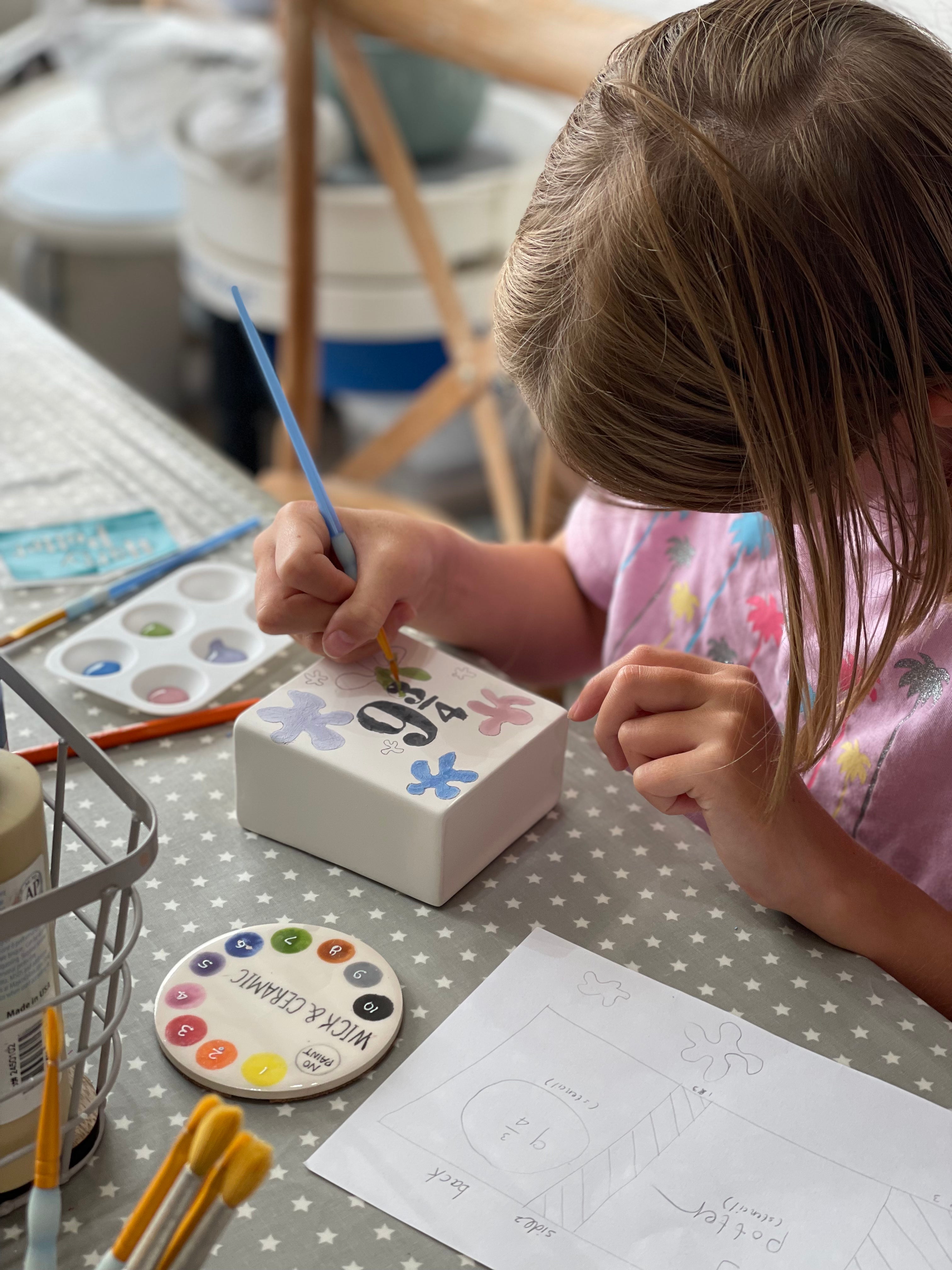 Child painting a ceramic box on a polka dot table with a colour chart at wick & ceramic in ickenham, london