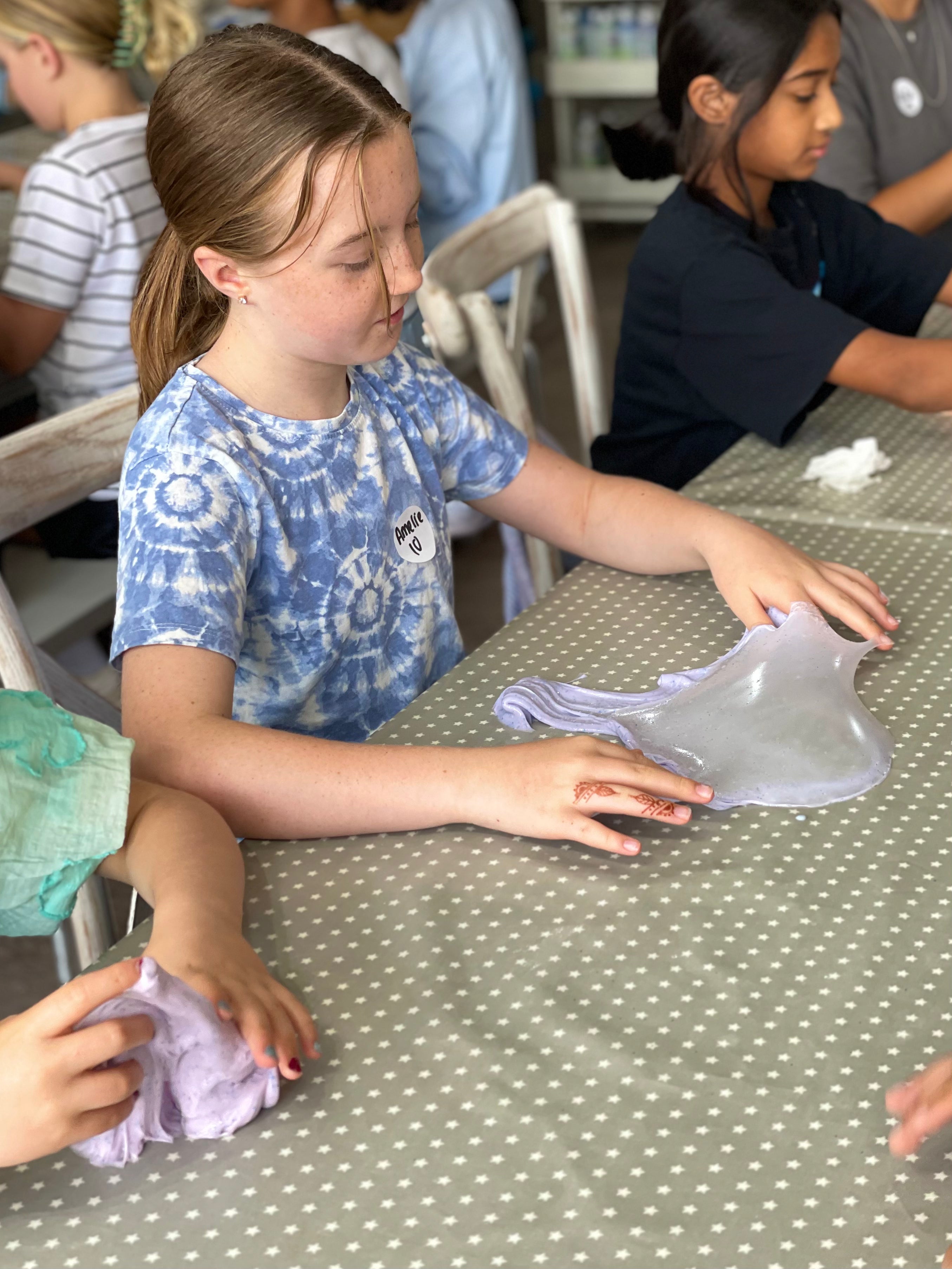 Children at a table with a polka dot tablecloth, playing with slime