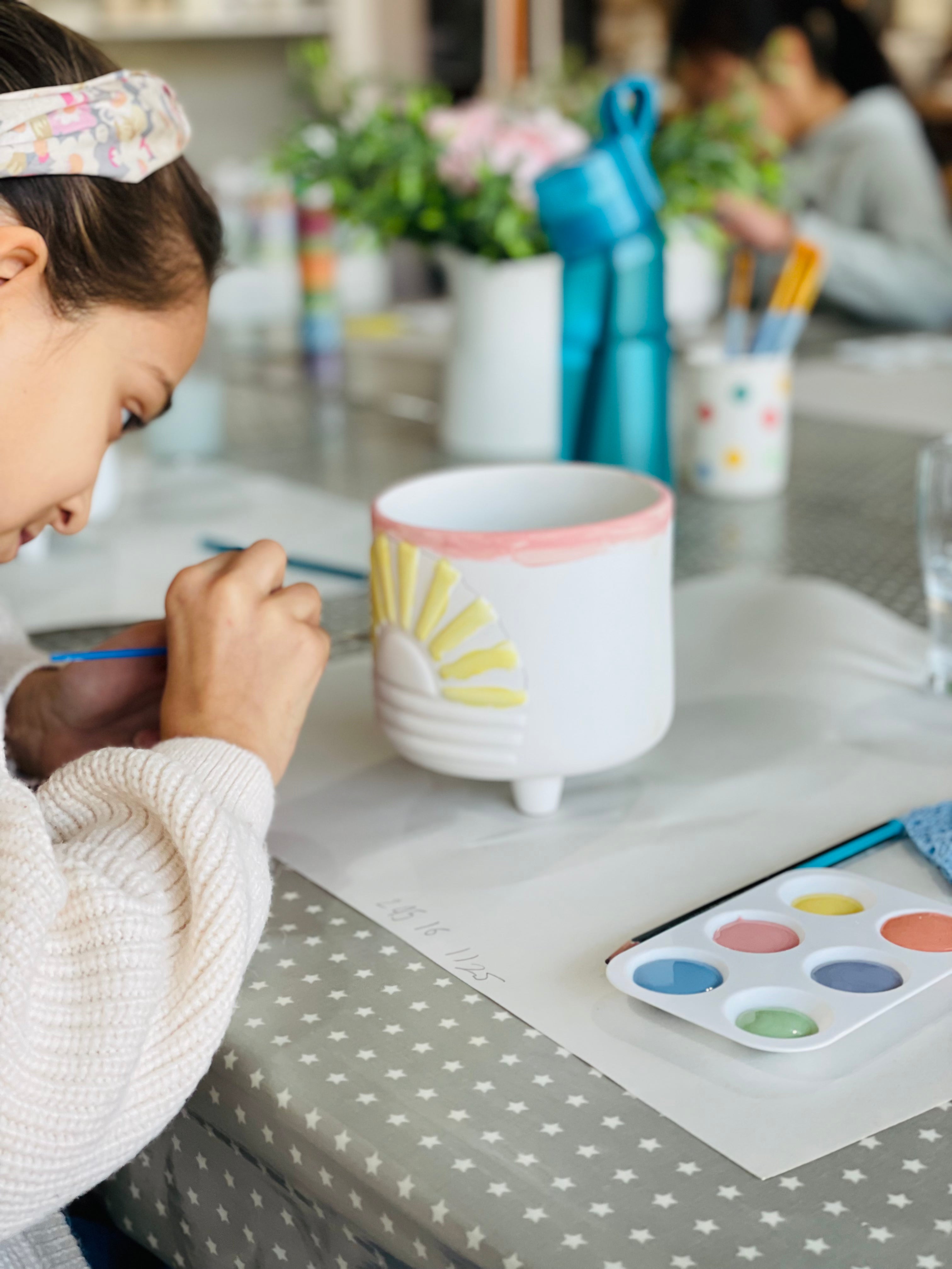 Child painting a ceramic mug with a sun design on a polka dot tablecloth.