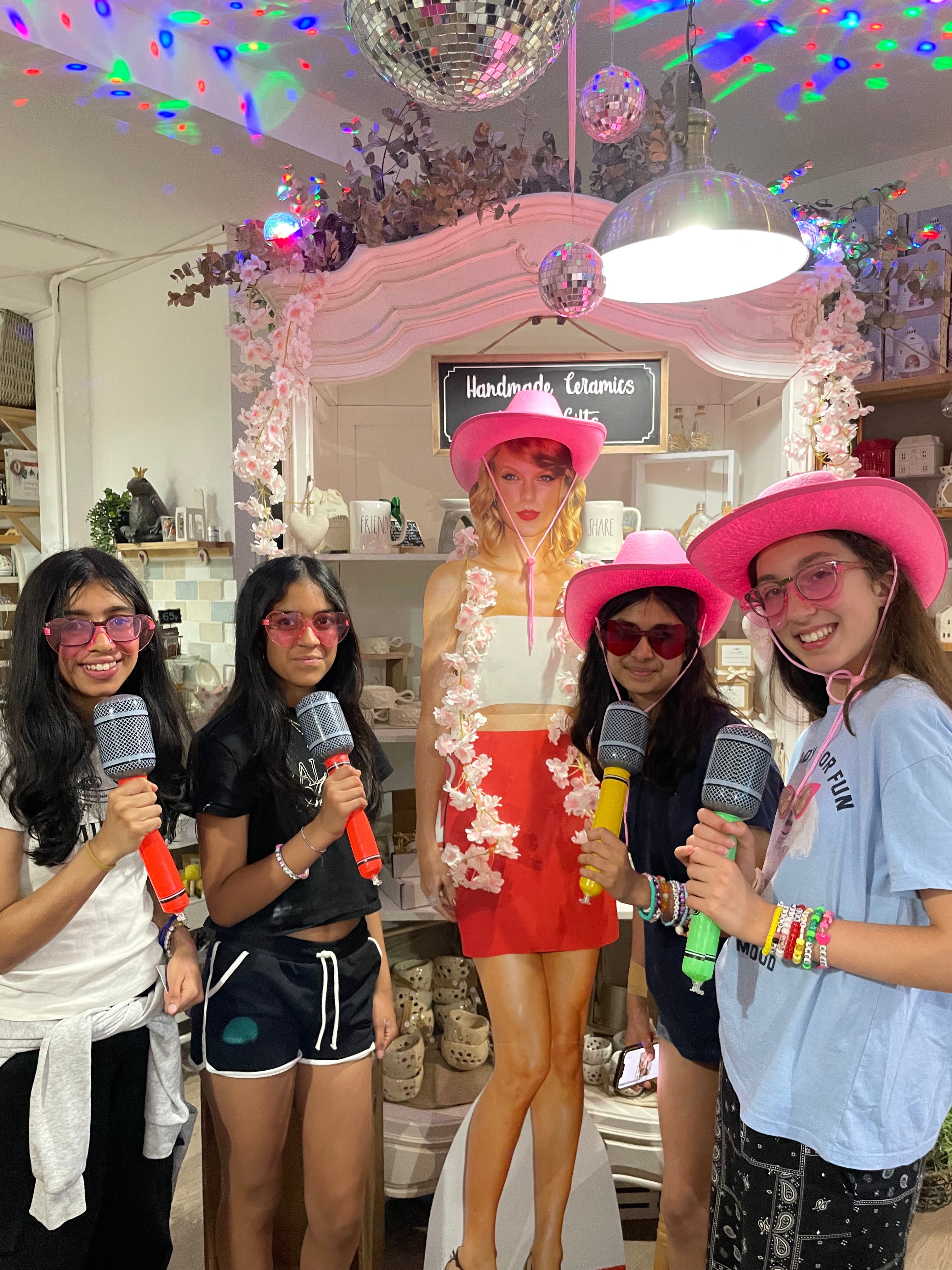 Group of four girls in pink cowboy hats and sunglasses holding microphones with taylor swift model at wick & ceramic ickenham london