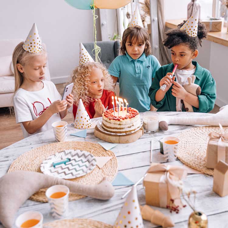 Children celebrating a birthday with a cake and presents in a room.