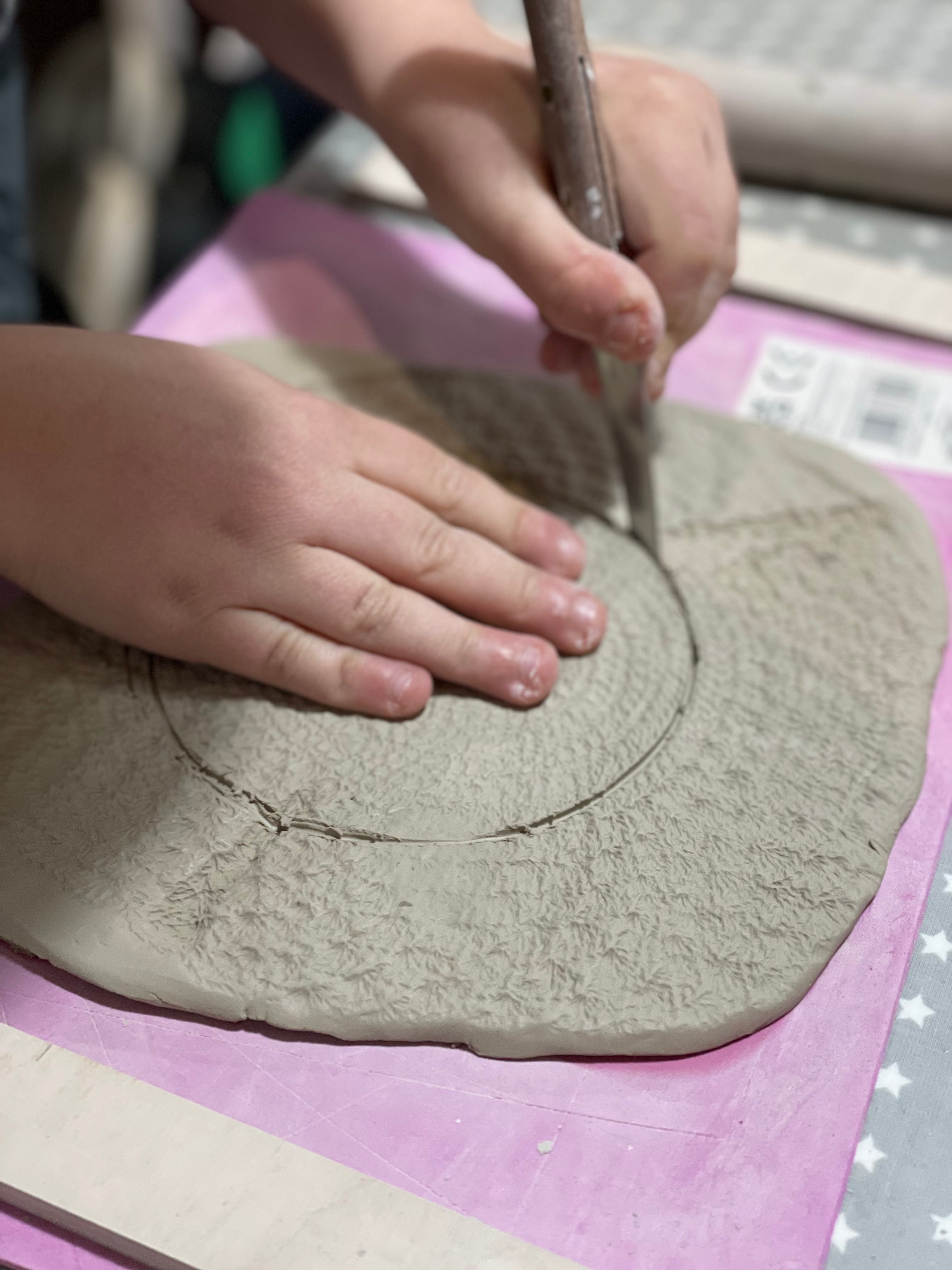 child cutting a circular piece of clay with sculpting knife on a pink surface