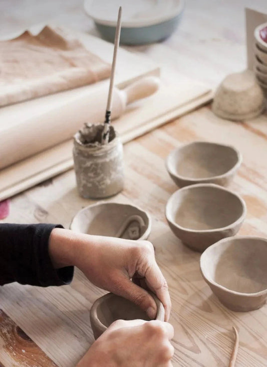 Person working on pottery with clay bowls on a wooden table wick & ceramic ickenham london