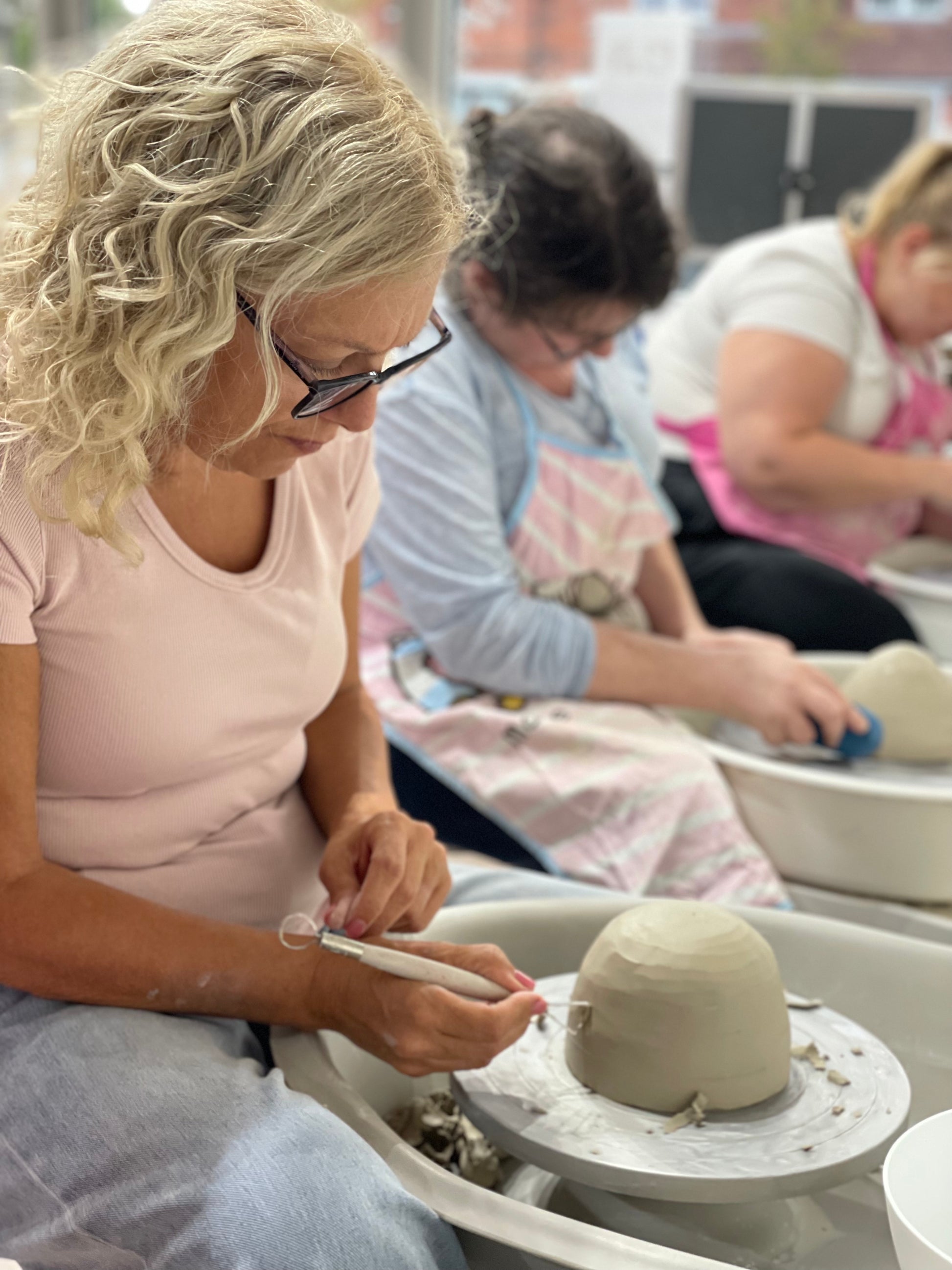 Blonde woman shaping clay on the pottery wheel during a Wick & Ceramic pottery making experience in Ickenham, London.