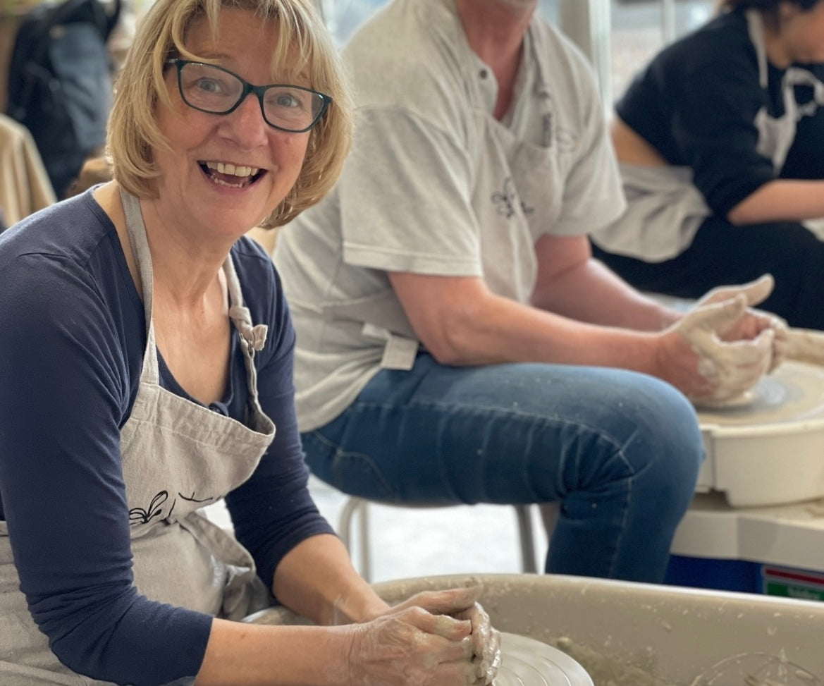 Lady smiling whilst pottery wheel throwing at Wick & Ceramic  in Ickenham, London.